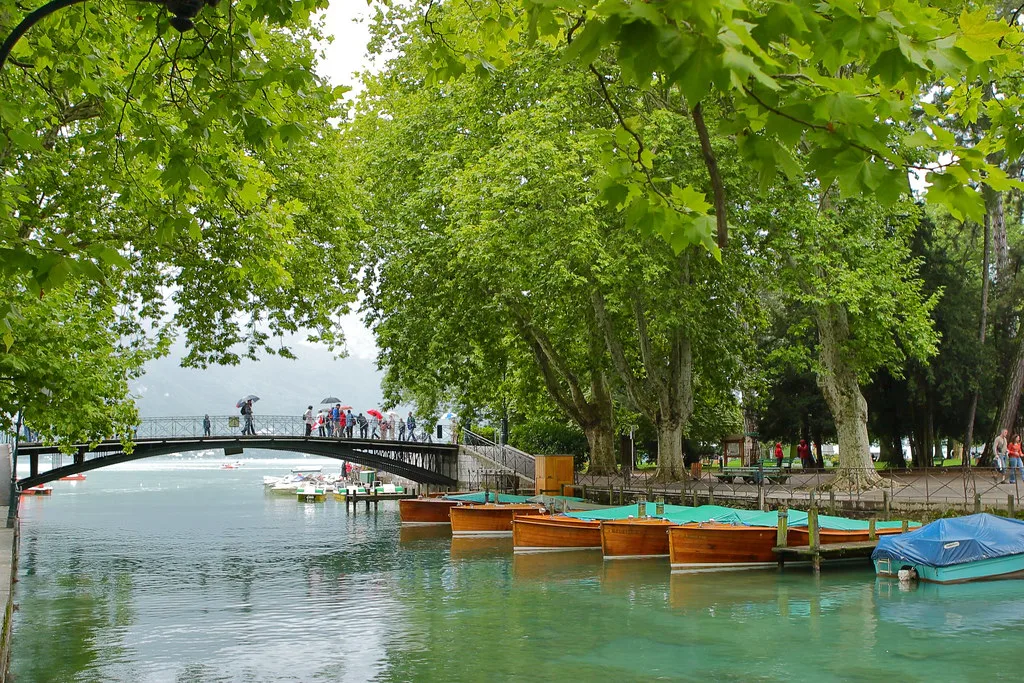 Venue view: the iron arch of the Pont des Amours on the tree-lined lakefront in Annecy, France. Resized and converted to WebP.